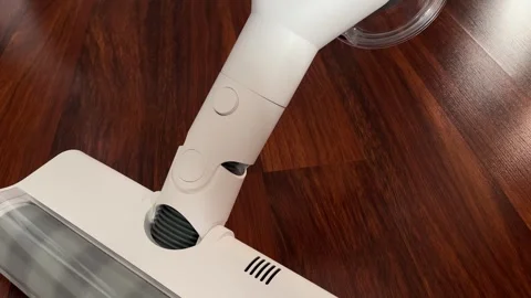 A modern white cordless vacuum cleaner glides smoothly over a dark wooden floor. Stock Footage 340194572