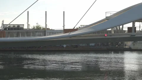 Modern white pedestrian bridge spanning calm water with urban background at suns Stock Footage 315737359