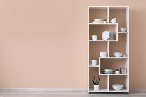 Modern white storage shelf with kitchenware and succulents against a peach wa Stock Photos