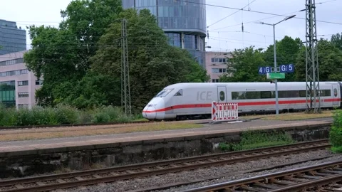 Modern white train passing by platform with green trees and glass skyscraper 스톡 동영상 337405095