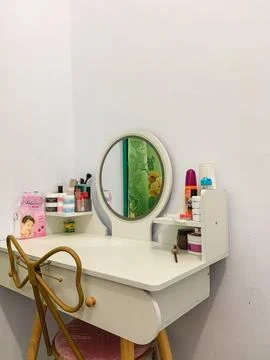 A modern white vanity table with a round mirror and cosmetics arranged in a.. Stock Photos