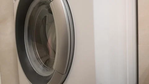 Modern White Washing Machine Close-up with Laundry Visible Inside Glass Door Stock Footage 339280722