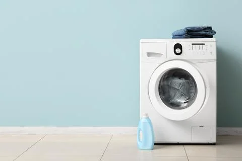 Modern white washing machine with laundry detergent and folded jeans on a lig Stock Photos