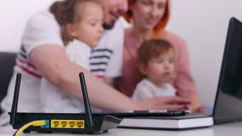 Modern wifi router on light table in the room. Mom and dad play on computer w 库存影片 131786689