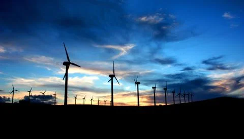 Modern windmill silhouettes during sunset with dark blue sky and clouds behind Stock Photos