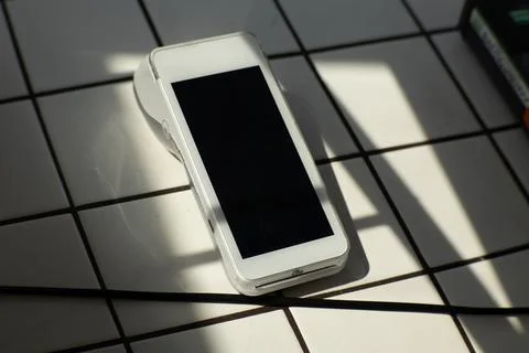 Modern wireless payment terminal placed on a tiled surface in natural light. Stock Photos