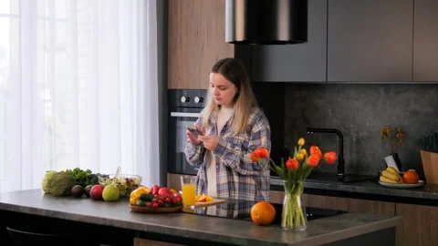 Modern woman prepares snack using smartphone in stylish kitchen. Smartphone Stock Footage 277621751