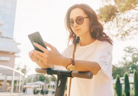 Modern woman using smartphone while standing with an electric scooter. Stock Photos