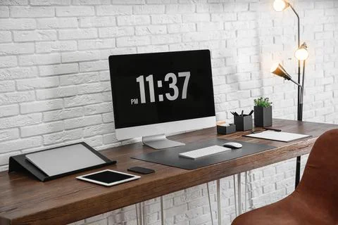 Modern workplace interior with computer and devices on table near brick wall Stock Photos
