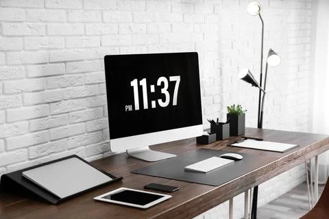 Modern workplace interior with computer and devices on table near brick wall Stock Photos