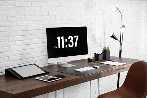 Modern workplace interior with computer and devices on table near brick wall Stock Photos