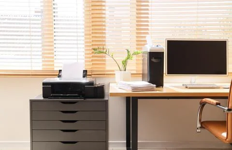 Modern workplace with shredder, documents and printer near window in office Stock Photos