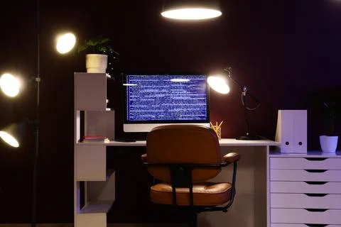 Modern workspace with computer displaying code and warm lighting Stock Photos
