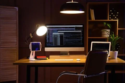 Modern workspace with computer screens displaying code at night 스톡 사진