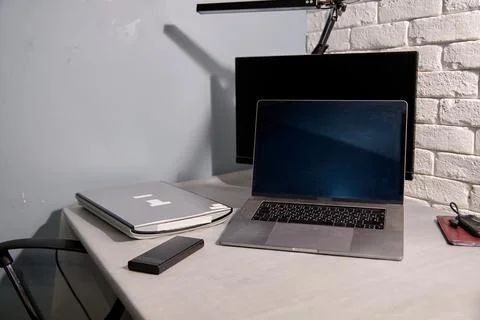 Modern workspace with laptop, closed notebook, external monitor, and brick .. Stock Photos