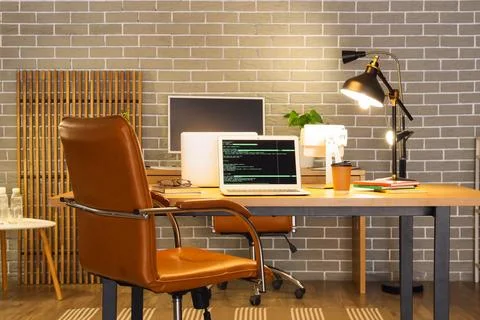 Modern workspace with laptop showing code and office chair 스톡 사진