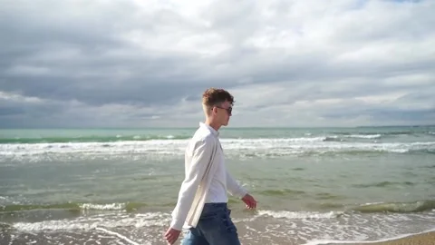 Modern young guy in a shirt walks along the sandy seashore, sunny day Video stock 167303683