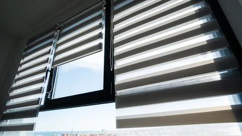 Modern zebra roller blinds filtering daylight on apartment window with city view Foto stock