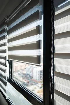 Modern zebra roller blinds filtering daylight on apartment window with city view Foto stock