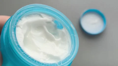 Moisturizer in a blue jar in a close-up in your hand, a lid on the table. Cream Stock Footage 324553901
