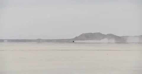 Mojave Dry Lake Bed Wide Shot Panning with Car Speeding Across Horizon Stock Footage 89941618