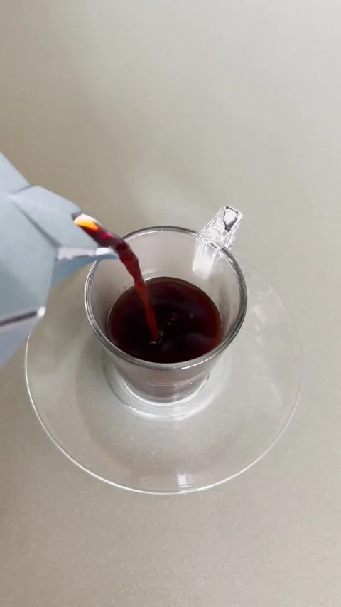 Moke pot coffee maker pouring hot espresso coffee into small glass or mug on Stock Footage 345518050