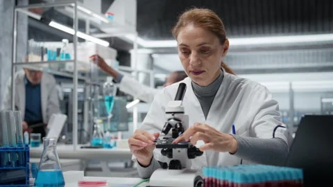 Molecular biologist using compound microscope for detailed cellular analysis Stock Footage 325748410