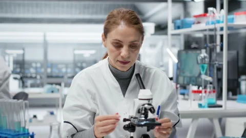 Molecular biologist using compound microscope for detailed cellular analysis Stock Footage 326703129