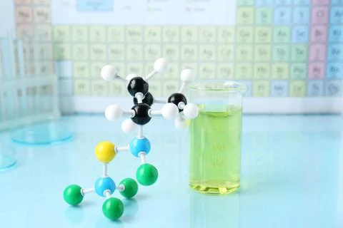 Molecular model and measuring cup on light surface against periodic table Foto stock