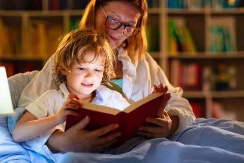 Mom and child reading book in bed. Kids read. Stock Photos