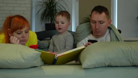 Mom and dad look at the screens of phones, the child independently reads a book Stock Footage 229546853