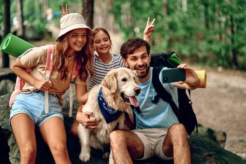 Mom and dad with their daughter with backpacks and a labrador dog take a self Stock Photos