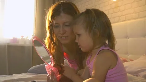 Mom and daughter are looking in the mirror on the bed in the bedroom Stock Footage