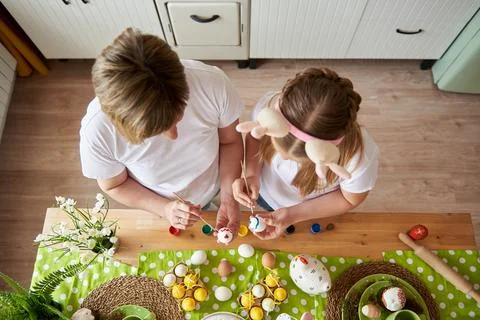 Mom and daughter are preparing for Easter and painting eggs with brushes, top Stock Photos
