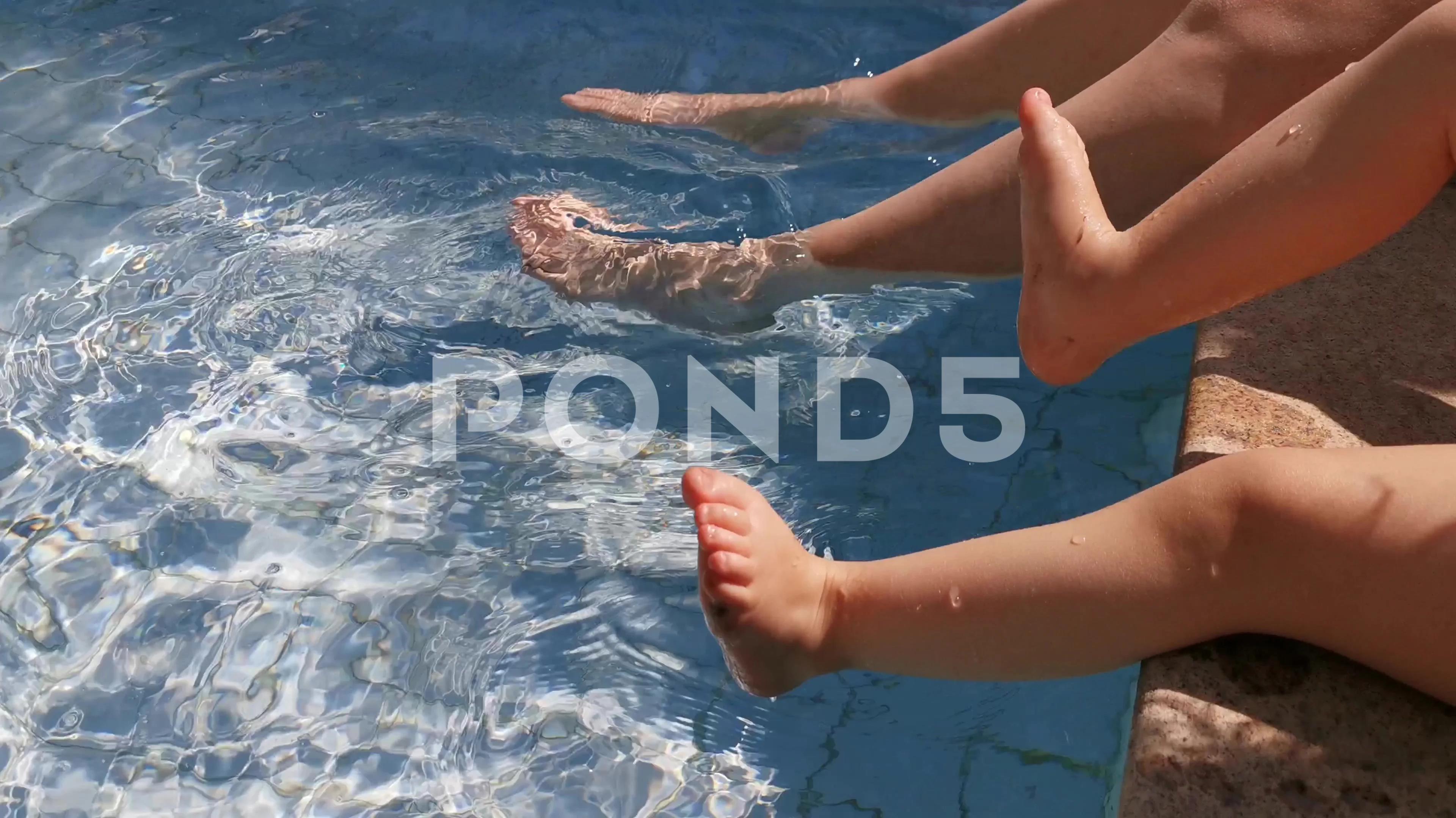 Mom and daughter playing with their feet on swimming pool