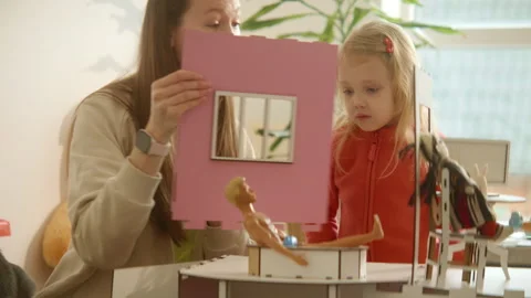 Mom and daughter in process of assembling wooden dolls house, pink barbie home Stock Footage 246851475