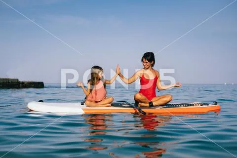 Mom and little daughter doing yoga on the paddle board Stock Photos