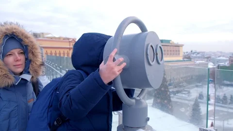 Mom and son looking through binoculars on roof of building in city in winter. Stock Footage 117618873