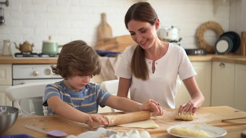 Mom and son work in kitchen lady looks at boy rolling dough Video stock 158980163