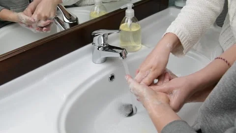 Mom assisting her kid while washing hands, rubbing fingers in bathroom at home Stock Footage 131557492