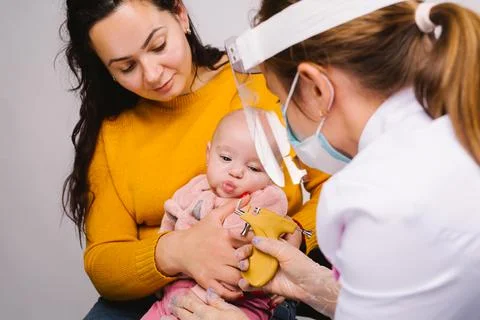 Mom with babygirl in her arms and a doctor in a medical mask and pandemic face Stock Photos