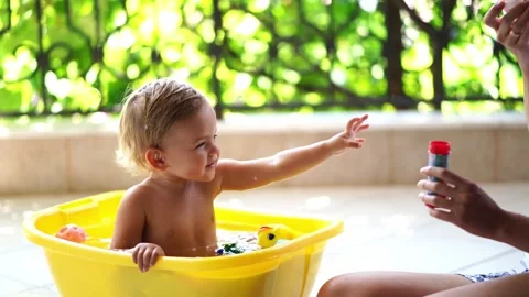 Mom blows soap bubbles on a little girl sitting in a bowl of water Stock Footage 279782353