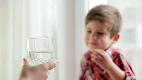 Mom bringing her thirsty son glass of water, little boy drinking water from Stock Footage