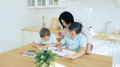 Mom helping two sons to draw with felt-tip pens on paper in the kitchen Stock Footage 118525918