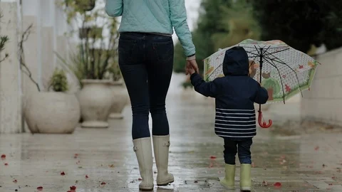 Mom with her son are walking in the rain in rubber boots and umbrellas. Stock Footage