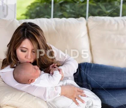 Mom kissing her infant son while resting on white sofa Stock Photos