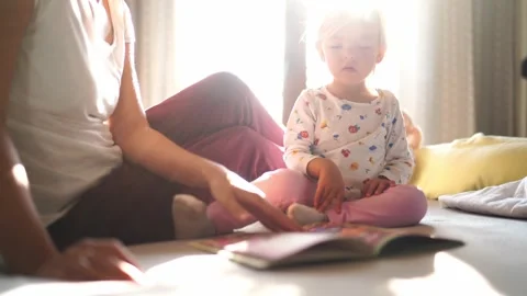 Mom leafing through a book in front of a little girl sitting on the bed Stock Footage 280194935