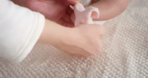 Mom lovingly puts pink socks on a newborn girl lying in diaper in a child crib Stock Footage 167325939