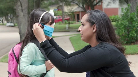 Mom puts mask on daughter before she walks to bus stop Stock Footage