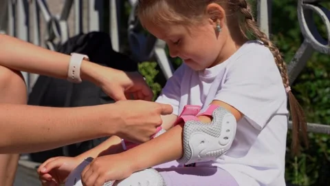 Mom putting on inline skates rollers elbow protection to daughter child in Stock Footage 237545965